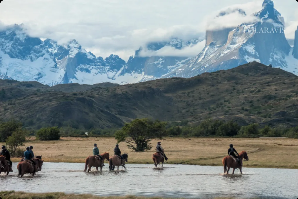 Grupo a caballo cruzando un vado frente a la cordillera fueguina