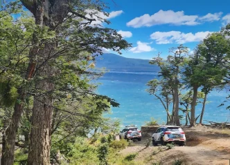 Dos vehículos 4x4 estacionados entre lengas frente a un lago