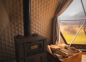 Interior de un domo con estufa a leña y ventanal al bosque