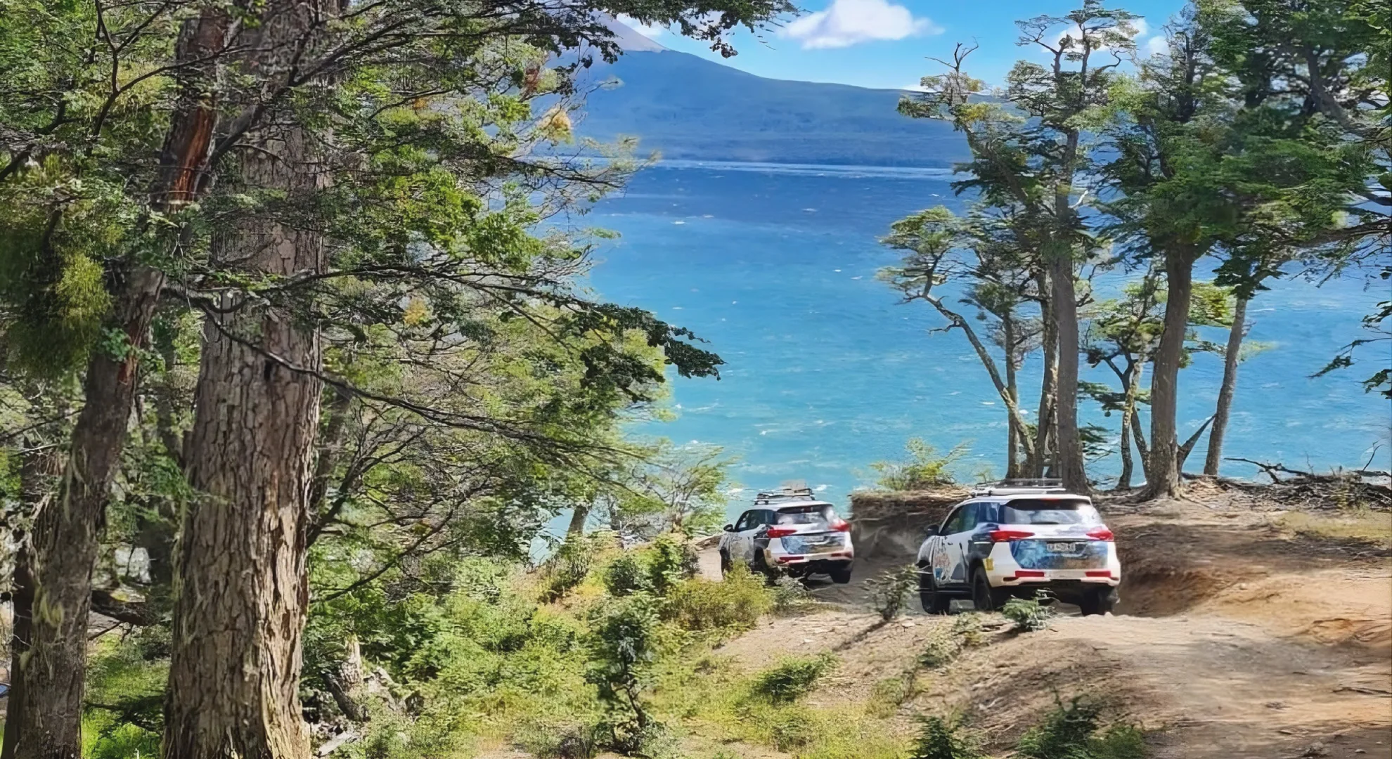 Dos vehiculos 4x4 entre el bosque, junto a un lago fueguino