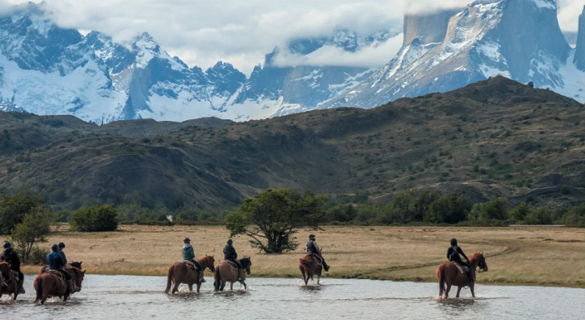 Grupo a caballo cruzando un valle con la cordillera de fondo