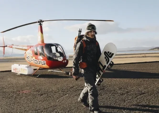 Pasajero con tabla de snowboard junto al helicóptero