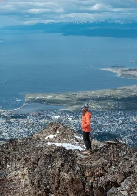 Persona en la cima de un mirador rocoso sobre la bahía de Ushuaia